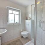 Bathroom with shower, toilet, and sink. Window with view outside.