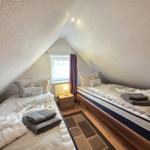 Two beds in attic room with window and nightstand.