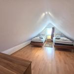 Two beds in an attic room with wooden floor and window.