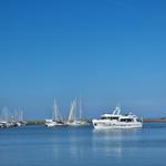 A white motorboat sails through a harbor with many sailboats.