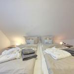 Two beds with bathrobes and towels under sloped ceiling