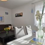 Living and dining area with sofa, table, and chairs. Window with white curtains.