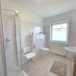Bathroom with shower, toilet, and sink. Window and radiator visible.