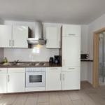 Kitchen with white cabinets, stove, and exhaust hood. Adjacent room is bathroom with shower.