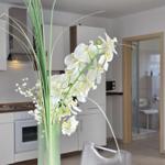 Kitchen with white cabinets and vase with white orchids. Passage to shower visible.