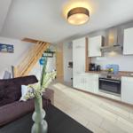 Living area with kitchen, sofa, and stairs to upper floor.