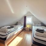 Two beds in an attic room with window and nightstand.