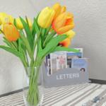 Tulips in vase on table with letter holder and tablecloth.