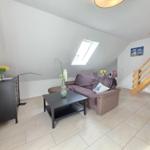 Living room with sofa, coffee table, and TV. Visible wooden staircase and skylight.