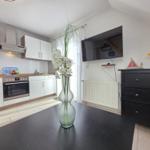 Kitchen with dining area, TV, and cabinet. Table with flower vase in foreground.
