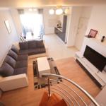 Wohnzimmer mit Sofa, TV und Küche im Hintergrund.