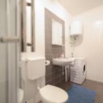 Badezimmer mit Toilette, Waschbecken, Spiegel und Waschmaschine.