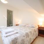 Schlafzimmer mit Bett, Nachttischen und Bad im Hintergrund.