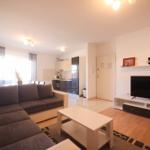 Wohnzimmer mit Sofa, Fernseher und Küche im Hintergrund.