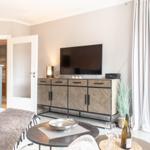 Wohnzimmer mit TV, Couch und Tisch. Durchgang zur Küche. Terrasse mit Blick.