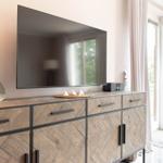 Flachbildfernseher über einem Holzschrank mit Schubladen und Türen. Durchgang zur Terrasse mit Blick auf Grün.