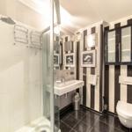 Badezimmer mit Dusche, Waschbecken und Toilette. Wand mit schwarz-weißen Streifen.