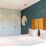 Schlafzimmer mit Bett, goldfarbenem Kopfteil und Kleiderschrank an der Wand.