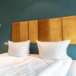 Schlafzimmer mit Bett, goldfarbenem Kopfteil und runden Spiegel an der Wand.