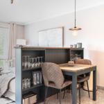 Essbereich mit Tisch, Stühlen und Gläsern. Im Hintergrund Wohnbereich mit Fenster.