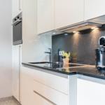 Moderne Küche mit weißen Schränken, schwarzer Arbeitsplatte und Edelstahlgeräten.