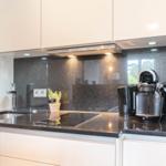 Moderne Küche mit schwarzer Arbeitsplatte und weißen Schränken. Darauf stehen Küchengeräte und eine Pflanze.