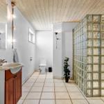 Bathroom with shower, toilet, and sink. Glass block wall and wooden ceiling.