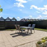 Terrace with table and chairs, surrounded by greenery and fence.
