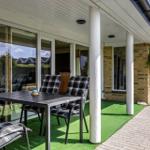 Terrace with table, chairs, and artificial grass. Background: house with glass front and pillars.