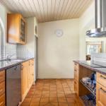 Kitchen with wooden cabinets, stone countertop, and terracotta floor. Window and range hood visible.