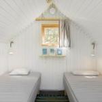 Two single beds in a room with white wood paneling and a window.