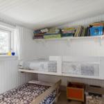 Room with bunk bed, lower bed, and shelf with books and games.