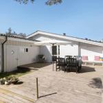 House with wooden terrace, garden furniture, and sun shade.