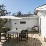 Deck with table, chairs, and umbrella. Background: white house and trees.