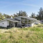 White vacation house with terrace, grill, and loungers in grassland.