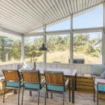 Terrace area with table, chairs, and bench. Large windows offer a view of the forest.