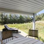 Deck with grill, lounge chair, and table. View of grassy slope and forest.