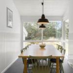 Dining room with wooden table, chairs, and large windows. Ceiling with wood paneling and pendant lamp.