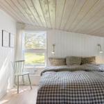 Bedroom with bed, window, and chair. Wooden ceiling and white walls.