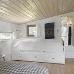 Bedroom with white bed, wooden ceiling, and windows. Hanging tapestry and mirror visible.