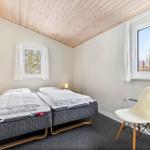 Two beds with mattresses, wooden ceiling, windows, and chair in room.