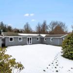 A gray house with a snow-covered yard and trees in the background.