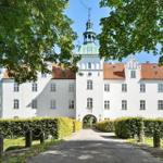 White castle with red roof and green dome, surrounded by trees and hedges.