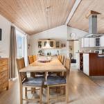 Dining area with wooden table, chairs, and kitchen with white cabinets.
