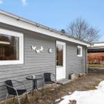 Gray wooden house with terrace, table, chairs, and snow on the ground.