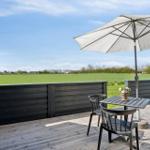 Terrasse mit Tisch, Stühlen und Sonnenschirm. Blick auf grünes Feld und Himmel.