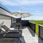 Terrasse mit Sonnenschirm, Tisch, Stühlen und Liegestühlen. Blick auf grünes Feld und Meer.