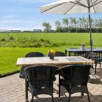 Terrasse mit Tisch, Stühlen und Sonnenschirm. Grüner Rasen und Felder im Hintergrund.