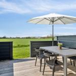 Terrasse mit Tisch, Stühlen und Sonnenschirm. Blick auf grünes Feld und Himmel.