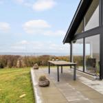 Terrasse mit Tisch und Blick aufs Meer. Glasfront führt ins Haus.